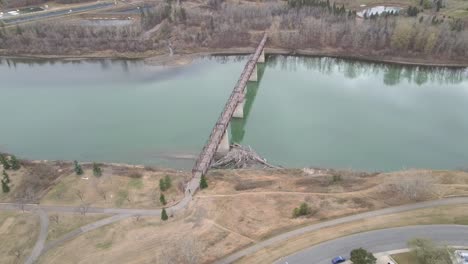 aerial-birds-eye-view-pan-out-over-poluted-North-Saskatchewan-river-at-Rundel-Park-past-an-empty-quiet-pedesterian-bridge-by-homes-during-COVID-19-restriction-where-social-distancing-is-practiced