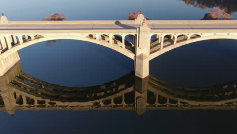 Cars-drive-on-bridge-over-dark-blue-river-water-with-beautiful-shadow-reflection-during-magic-hour