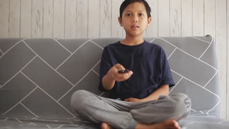 Un-Niño-Asiático-Viendo-Televisión-Y-Cambiando-De-Canal-Usando-El-Control-Remoto