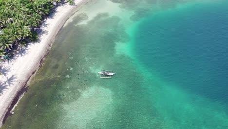 Aerial-top-view-over-the-turquoise-sea-in-the-Philippines-with-an-island-hopping-boat-floating-near-the-coastline-above-a-coral-reef,-travel-concept