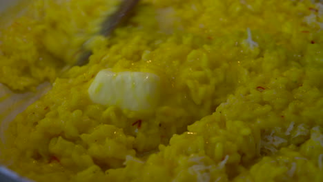 Mixing-creamy-yellow-saffron-risotto-with-a-knob-of-butter-melting-in-the-centre