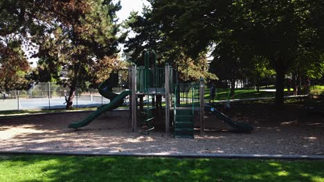 empty-playgroud-with-signage-prohibitting-children-and-lockdown-COVID-19-restrictions-of-social-distancing-pandemic-in-a-lush-green-summer-park-with-active-people-playing-tennis-in-the-background-1-2