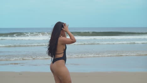 Hispanisches-Mädchen-Geht-Am-Strand-Entlang,-Im-Hintergrund-Brechen-Die-Wellen-Und-Ihr-Haar-Fließt-Im-Wind
