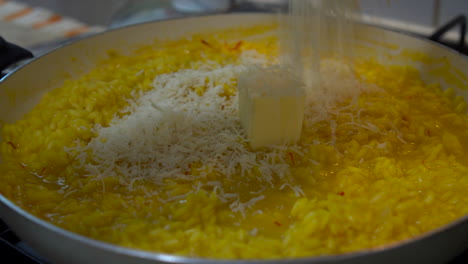 Chef-adding-butter-and-freshly-grated-parmesan-cheese-to-a-yellow-saffron-risotto