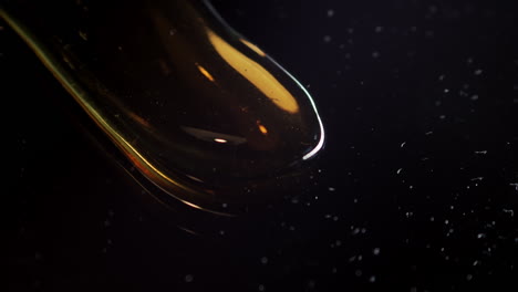 Oil-drop-flowing-on-black-background,-viscosity-concept,-extreme-closeup