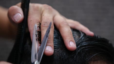 Close-up-of-a-barber-cutting-a-man's-hair-with-comb-and-scissors