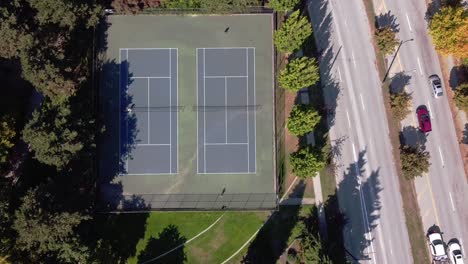 2-2-Aerial-dolly-roll-down-from-an-empty-bridge-road-with-a-car-next-to-uptown-Granville-Island-next-to-a-lush-green-park-in-a-birds-eye-view-tennis-courts-as-park-is-empty-and-people-playing-tennis