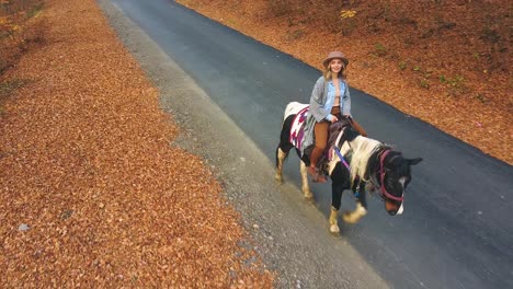 Girl-riding-a-horse-on-a-countryside-road-with-orange-leaves-on-the-ground