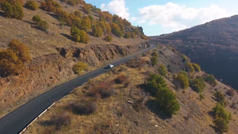 Drone-shot-of-a-car-driving-on-an-open-road-in-the-mountains