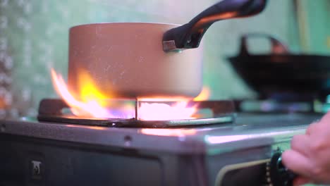 Kitchen-one-small-burner-turning-on-stove,-cooking-home-flame,-hand-turns-natural-gas-with-pan