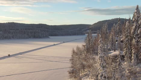 Schöne-Winterlandschaft-Mit-Skifahrern-Auf-Einem-Zugefrorenen-See,-Luftaufnahme-Mit-Bäumen-In-Der-Nähe-Und-Bergen-Im-Hintergrund
