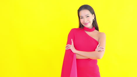 A-smiling-young-woman-against-a-sold-colored-background-standing-with-arms-crossed-in-front-of-her