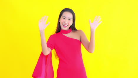 Young-Asian-woman-greets-in-elegant-fuchsia-dress-with-yellow-screen-in-background