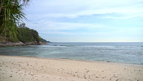 Tropical-island-beach-view-with-lush-green-landscape-beside-sandy-beach-and-clear-blue-ocean