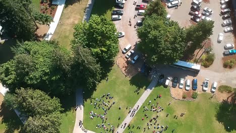 Aerial-birds-eye-view-over-lush-green-summer-camp-entrance-where-campers-await-parents-to-arrive-to-take-them-home-while-others-are-registering-to-start-the-new-week-of-fun-outdoor-fitness-adventure
