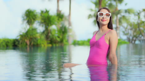 Young-Asian-girl-with-sunglasses-and-pink-swimsuit-relaxing-in-pool-alone