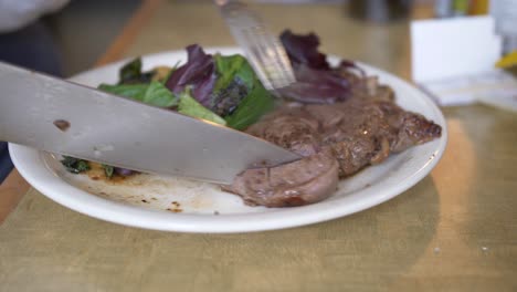 Schneiden-Eines-Steaks-Auf-Einem-Teller-Mit-Grünem-Salat