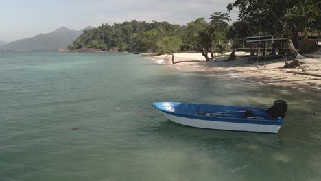 static-shot-of-small-boat-moored-on-a-tropical-beach-with-mountains-jungle