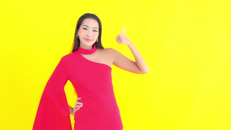 A-pretty-young-woman-against-a-solid-background-in-a-red-dress-gives-the-thumbs-up-for-success