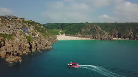 Tour-boat-off-Porthcurno-Beach,-Cornwall-coast-in-summer,-aerial-view