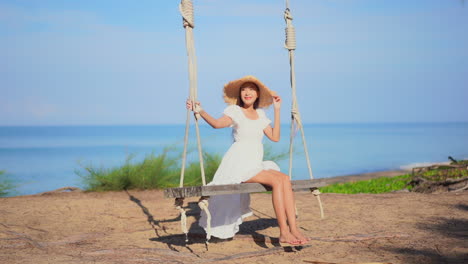 Young-woman-with-big-straw-hat-on-swing-and-sea-in-background