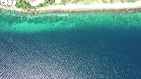 Aerial-wide-bird's-eye-view-over-a-coral-reef-in-transparent-turquoise-waters-near-a-green-coastline,-tilt-up-establishing-shot,-travel-concept