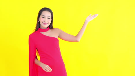 A-sophisticated-young-woman-in-a-red-dress,-gestures-with-her-hand-and-arm,-palm-up-to-copy-space