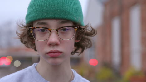 Teen-boy-outside-in-a-green-hat-and-glasses-looks-at-camera