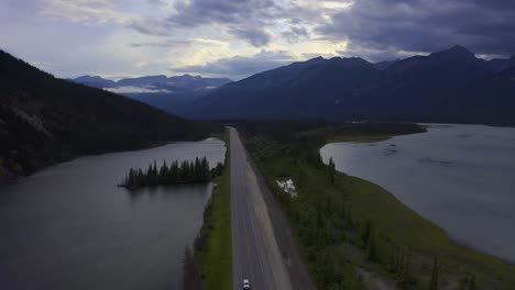 Twilight-summer-aerial-panout-over-highway-freeway-road-within-mountain-valley-dividing-lakes-marshes-with-some-clear-skies-partial-clouds-with-RV-travellers-at-birds-eye-view-lush-green-beaches-1-2