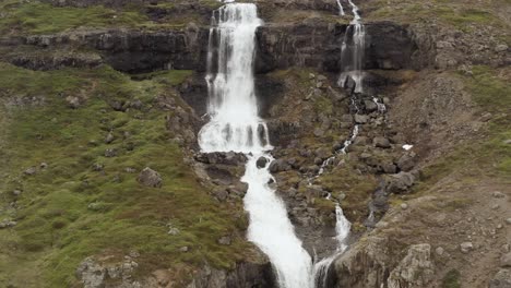 Majestic-waterfall-flows-down-rocky-cliff-in-wild-Iceland-landscape,-aerial
