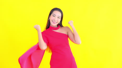 Happy-Asian-woman-exults-in-elegant-fuchsia-dress-with-yellow-screen-in-background