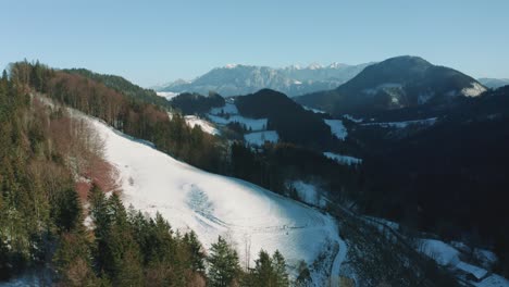 Aerial-drone-flight-moving-above-snowy-hills-and-green-tree-tops-in-the-Bavarian-Alps-in-winter-in-Germany,-close-to-Austria