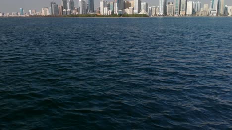 Un-Dron-Aéreo-Vuela-Sobre-El-Lago-Khalid-De-Sharjah-Hacia-El-Futurista-Distrito-De-Al-Majaz-En-Un-Hermoso-Día,-Modernos-Rascacielos-Residenciales-En-Los-Emiratos-árabes-Unidos