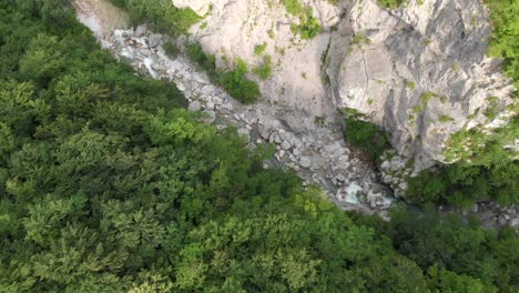 Drone-lifts-above-secluded-canyon-with-wild-river-and-big-rocks-in-summer