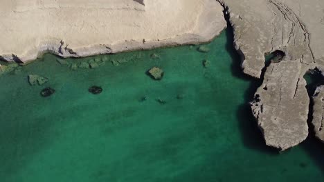 Two-people-diving-on-the-turquoise-water-of-patagonian-sea,-revealing-a-beautiful-landscape---Aerial-reveal-shot