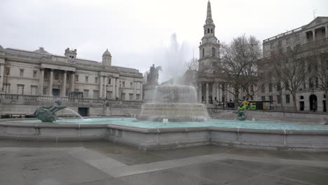Zeitlupenaufnahme-Eines-Der-Springbrunnen-Des-Trafalgar-Square,-Der-King-George-Statue-Und-Eines-Vorbeifahrenden-Krankenwagens