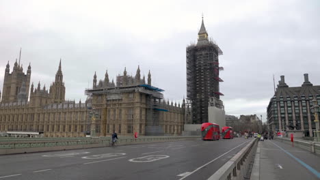 Static-shot-of-the-Big-Ben-surrounded-by-scaffolding,-parliament-palace-and-double-decker-buses