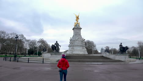Static-shot-of-young-woman-with-red-jacket-walking-in-an-empty-Buckingham-Palace-square,-no-tourists