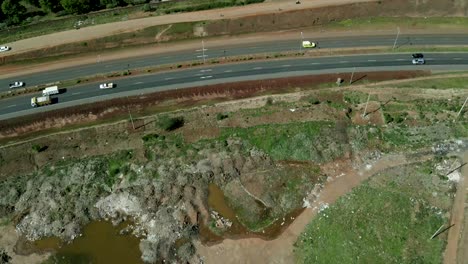 Charco-Estancado-De-Agua-Sucia-En-Un-Vertedero-Que-Bordea-La-Carretera-Africana-Con-Tráfico-En-Kenia,-áfrica