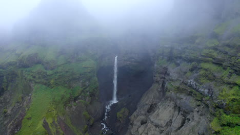 Drone-footage-of-Hangandifoss-waterfall-in-Mulagljufur-canyon,-with-foggy-cloudy-conditions-in-Iceland