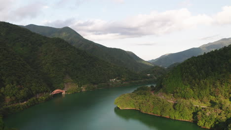 Calm-Waters-Of-Lake-Okutama-With-Mugiyama-Bridge-And-Green-Mountains-On-A-Sunny-Day-In-Okutama,-Japan