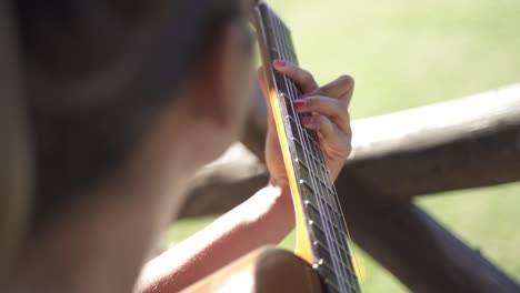 Young-female-kindly-playing-guitar-outdoors-daylight-closeup-slow-motion-and-60fps