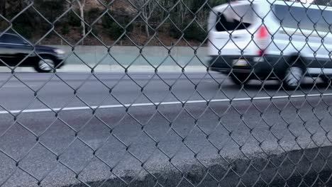 Vehicles-driving-on-busy-freeway,-abstract-view-through-chainlink-fence