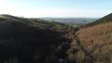 Coed-Llangwyfan-Welsh-woodland-valley-national-park-aerial-view-descending-right-across-sunrise-countryside