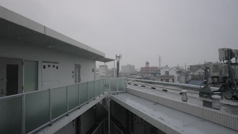 Balcony-Of-An-Apartment-Building-With-Cityscape-In-Background-During-Snowfall-Winter-Season-In-Tokyo,-Japan