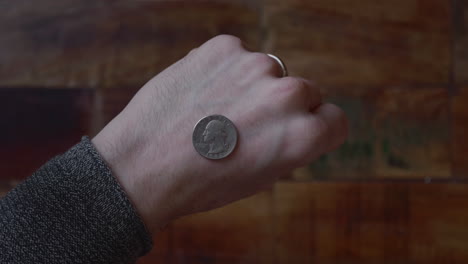 Man-Reveals-The-Coin-At-The-Back-Of-His-Hand-with-Wooden-Floor-On-The-Background