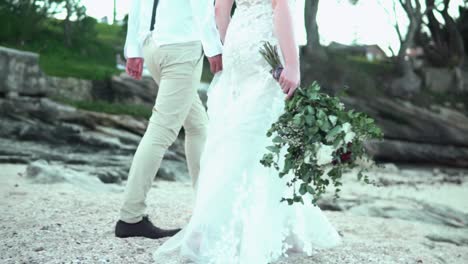 Braut-Und-Bräutigam-Gehen-Am-Strand-Spazieren,-Braut-Hat-Blumen-In-Der-Hand---Zeitlupe