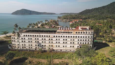 Empty-coastal-beach,-abandoned-white-resort-hotel-,-Drone-orbiting-the-white-resort-hotel-in-the-coastal-lagoon