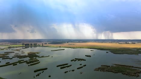 Aerial-elevation-shot-of-wetlands-and-vast-farm-field-with-distant-storm