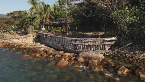 Abandoned-wooden-skeleton-of-a-boat-on-the-coastal-rocky-beach-of-the-ocean